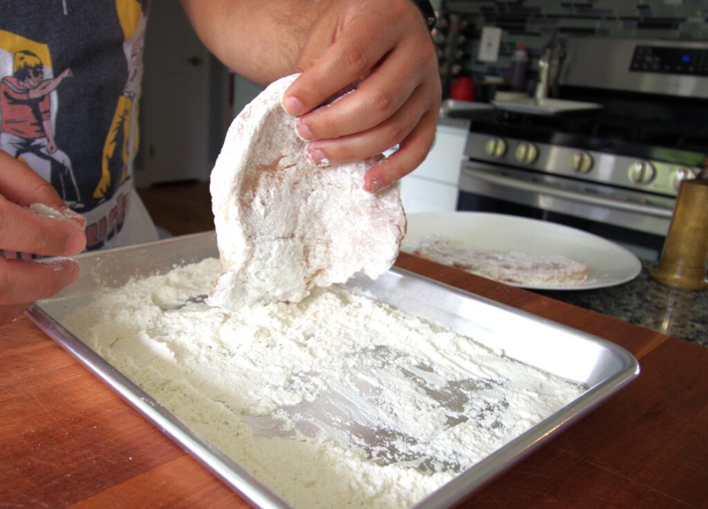 hands dredging a pork chop in flour