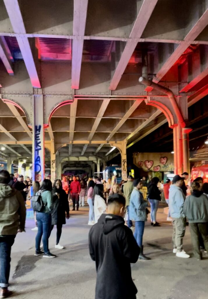 Trusses under a bridge lit up with rainbow lights and crowds of people underneath
