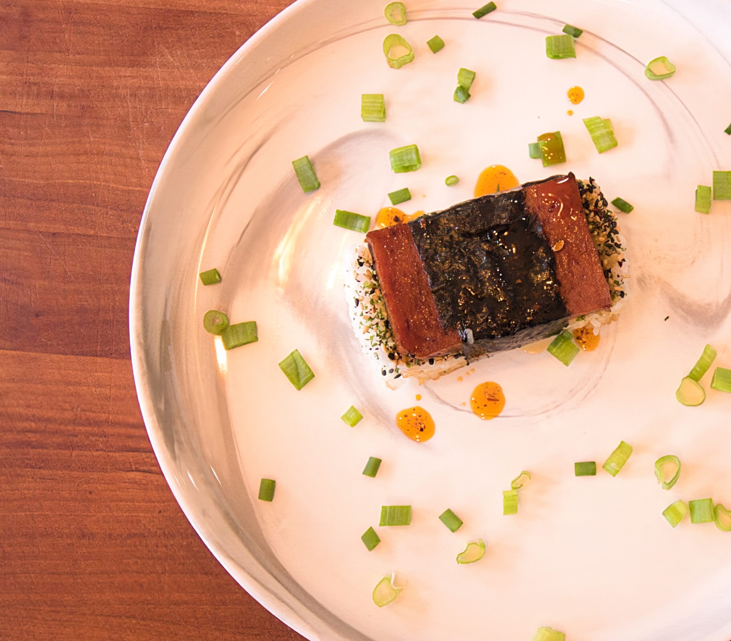 spam musubi on a white plate with scallions around it