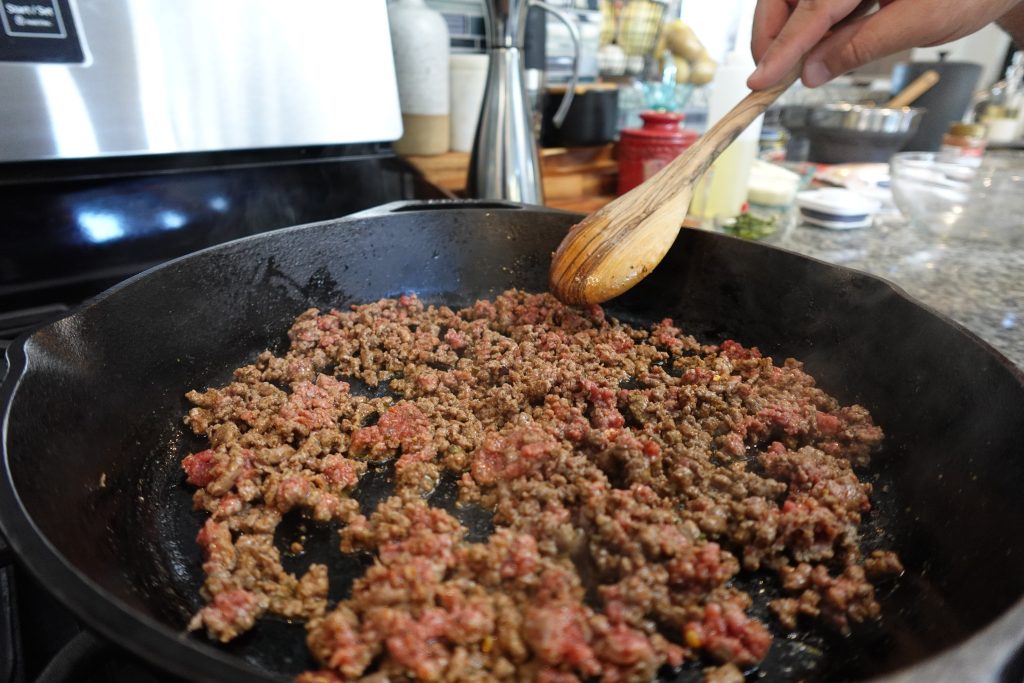 Ground beef cooking in cast iron skillet for beef crispitos.