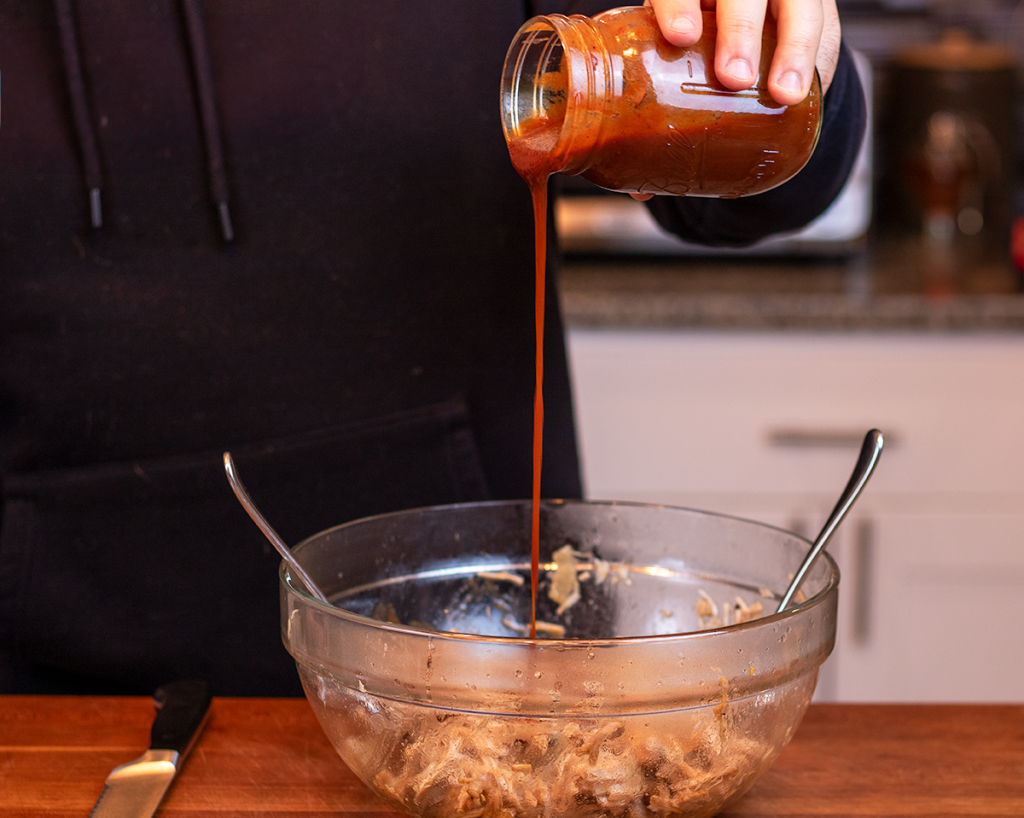 Pouring BBQ sauce over pulled pork in a bowl.